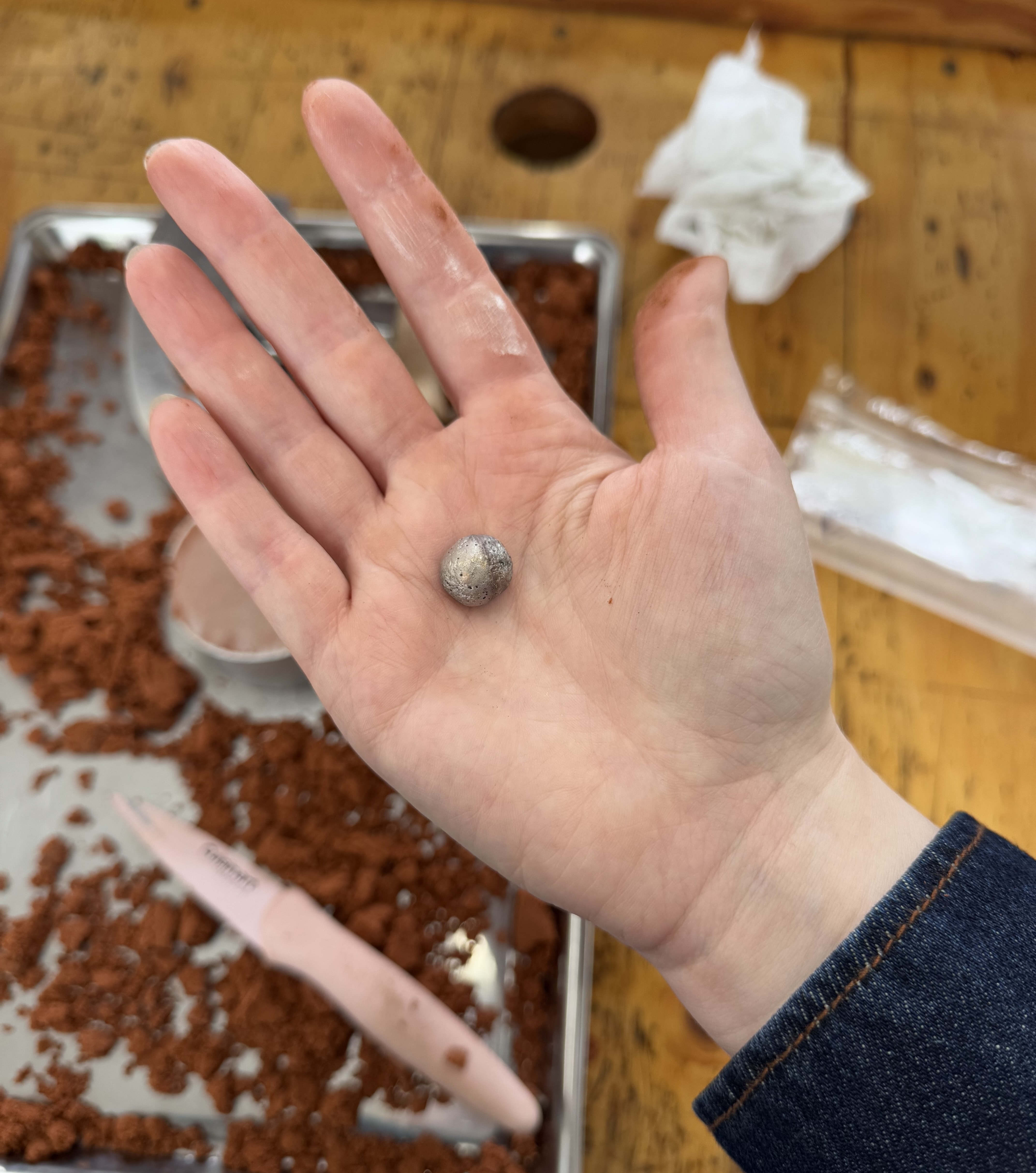 small silver bead in the palm of a hand with sand in the background