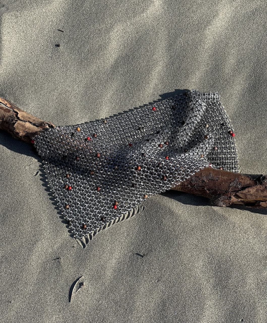 glass beaded fabric resting on top of driftwood in the sand